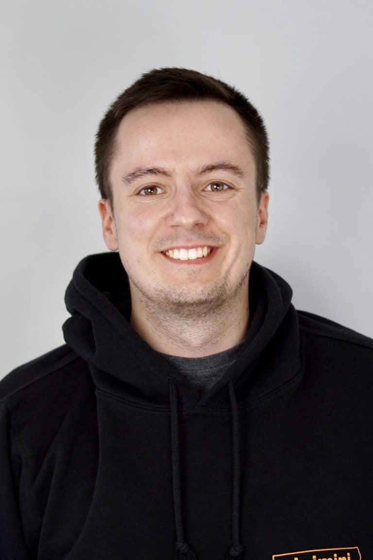 Portraitfoto von einem Mann mit kurzen braunen Haarren. Er lächelt und trägt einen schwarzen Hoodie mit claimini Logo