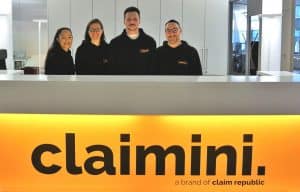 Bild von vier Mitarbeitern am Empfangstresen mit dem claimini logo. Im Hintergrund sieht man die Büroräume.