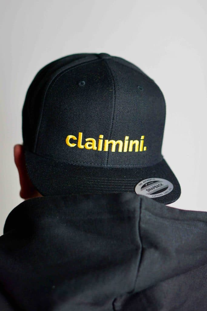 Ein Mann trägt eine Schwarze snap back Kappe mit gelbem claimini Schriftzug