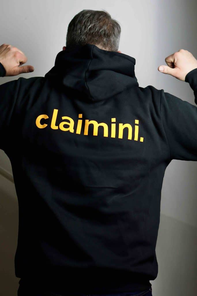 Ein Mann trägt einen schwarzen Hoodie mit einem gelben claimini Schriftzug auf dem Rücken